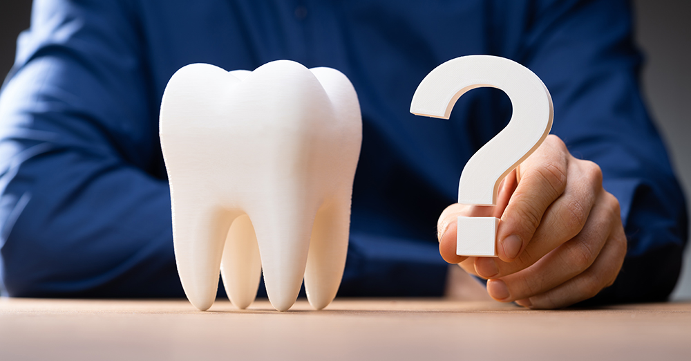 Tooth model next to a hand holding a question mark