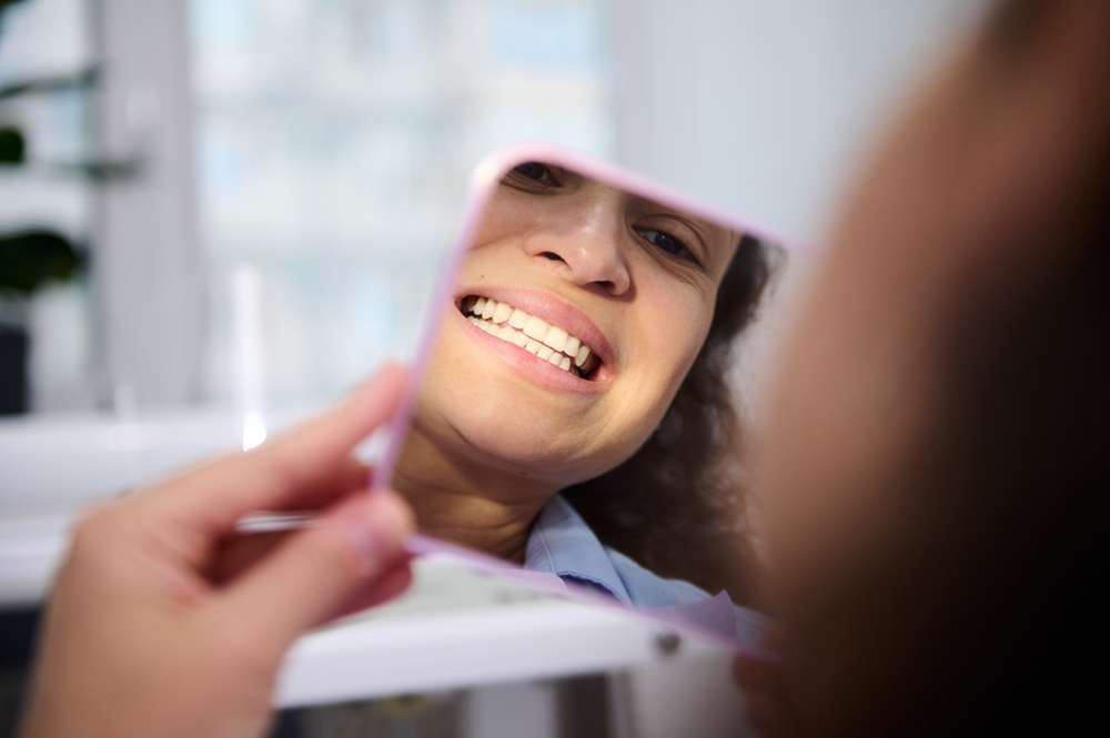Female patient checking her smile in a mirror after reconstructive dental treatment