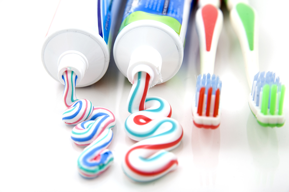 Two toothpaste tubes with toothpaste coming out next to toothbrushes